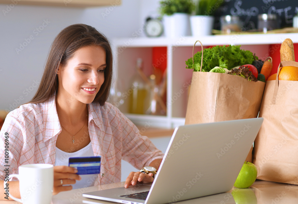 Smiling woman online shopping using tablet and credit card in kitchen Smiling woman online shopping using tablet and credit card in kitchen