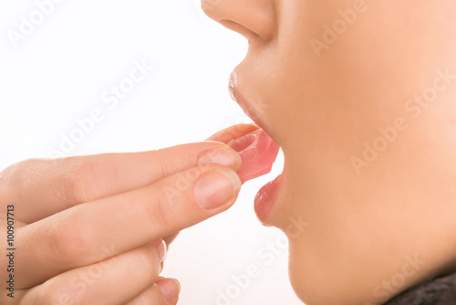 Young girl bringing red pill to her mouth.