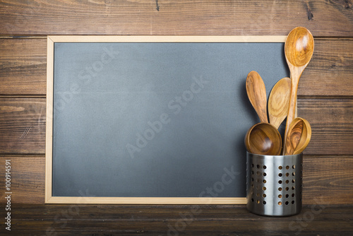 Pizarra vacía con espacio para texto sobre fondo de madera y utensilios de cocina