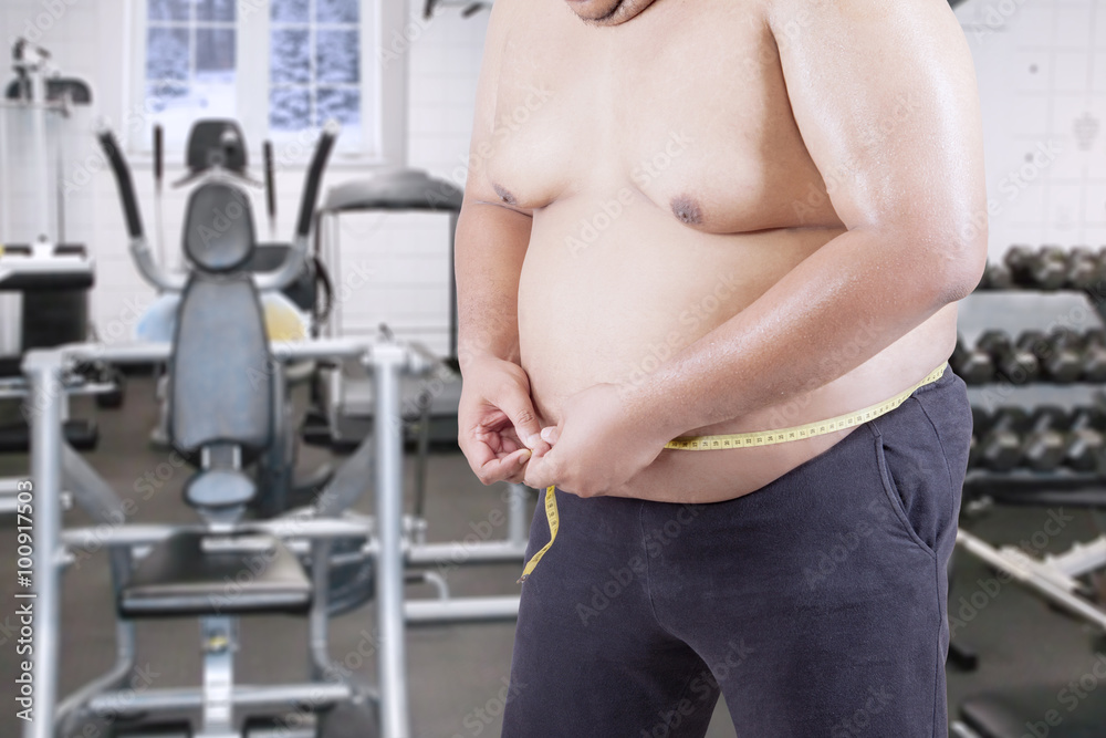 Overweight man measuring his belly at gym