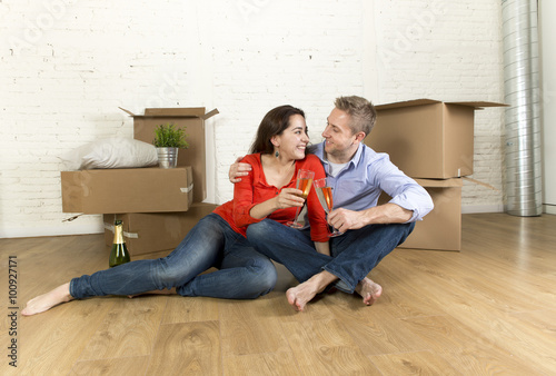 happy American couple sitting on floor unpacking together celebrating with champagne toast moving in a new house