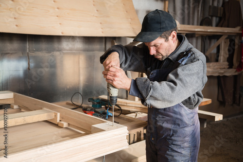 Carpenter assembles wooden furniture, focus on the hand drill