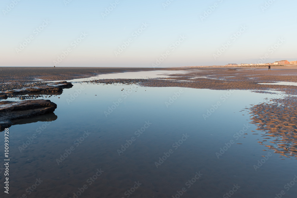 Beautiful sunny winters day on a british beach, with sand ripples and the sky reflecting in a water pool.