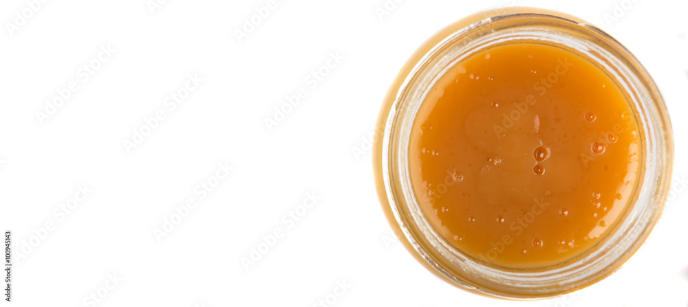 Orange fruit curd in glass jar over white background