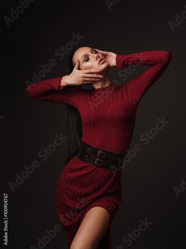 The slim model in the marsala dress with slicked straight black ponytail is demonstrating the new trendy fashion collection in the studio