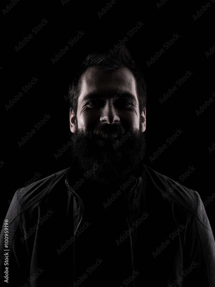 Desaturated laughing man looking at camera. High contrast low key dark shadow portrait isolated over black background.