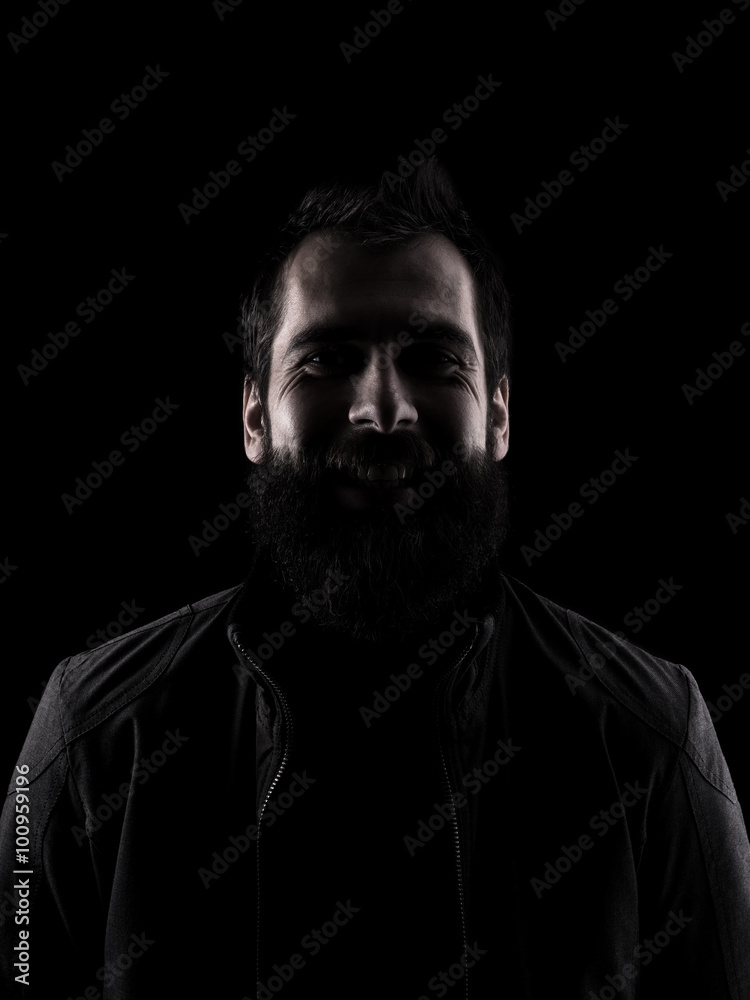 Desaturated laughing man looking at camera. High contrast low key dark shadow portrait isolated over black background. Desaturated laughing man looking at camera. High contrast low key dark shadow portrait isolated over black background.