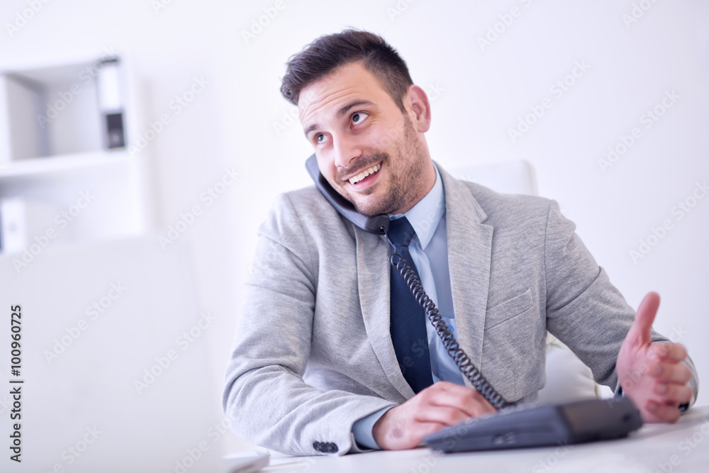 Naklejka premium Businessman on phone while using laptop in the office