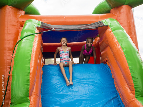 Foto Happy little girls sliding down an inflatable bounce house
