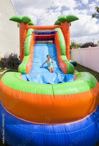 Slika na platnu Smiling little girl playing on an inflatable slide bounce house outdoors