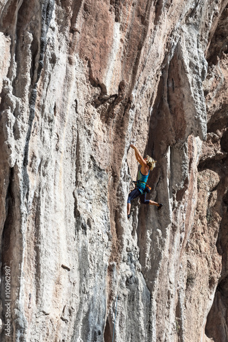 Blond Female Climber ascending Vertical Orange Rock