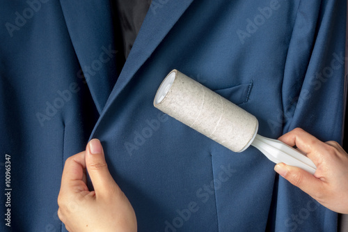 Dry cleaning and business theme: a man hand with blue suit holding a white sticky brush for cleaning clothes and furniture from dust