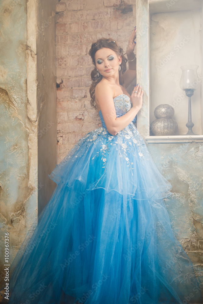 Beautiful young woman in gorgeous blue long dress like Cinderella with perfect make-up and hair style