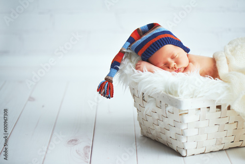 Cute newborn baby in blue knit cap sleeping in basket