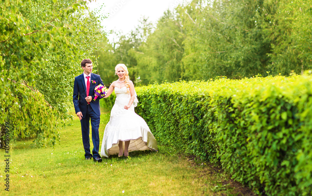 Obraz premium Bride and groom walking in summer park outdoors