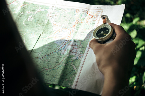 traveler exploring map with compass in sunny forest in the mount photo