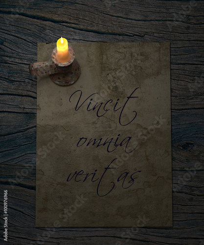 Vincit omnia veritas latin proverb. Truth conquers all. Old paper and candle on rustic wooden table. photo