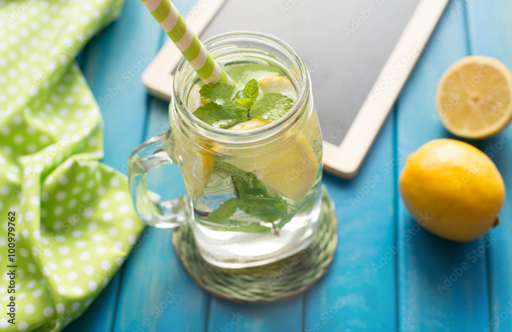 Lemonade with lemon slices and mint in a jar mug with straw on blue wooden background from top view. Water with lemon. Detox. Lemonade with lemon slices and mint in a jar mug with straw on blue wooden background from top view. Water with lemon. Detox.