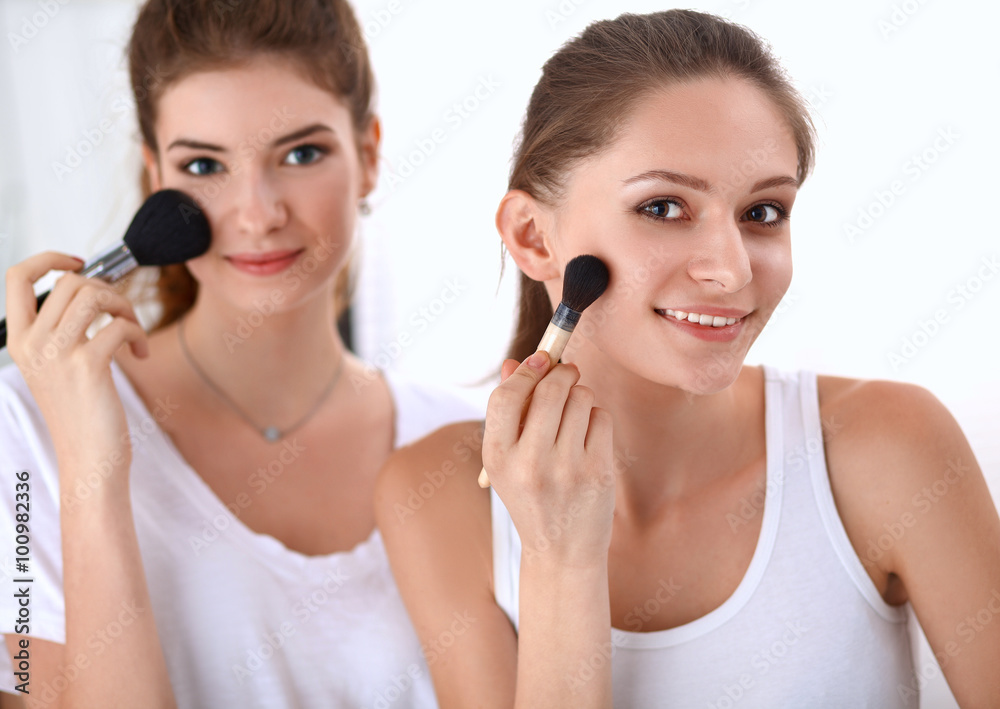 Beautiful girls looking in the mirror and applying cosmetic with a big brush Beautiful girls looking in the mirror and applying cosmetic with a big brush