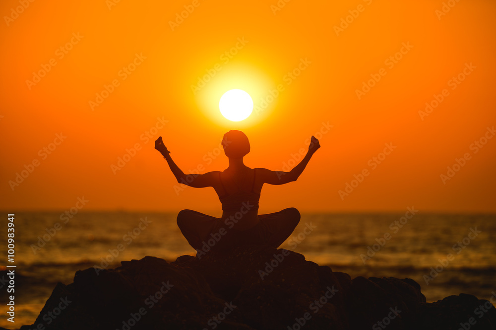 Female meditates during yoga in the sunset
