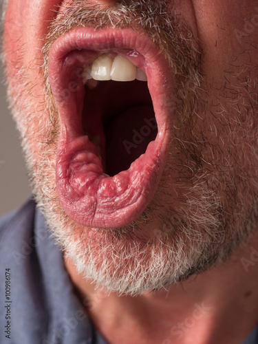 Close up photograph of a man's mouth yelling angrily with pursed lips.