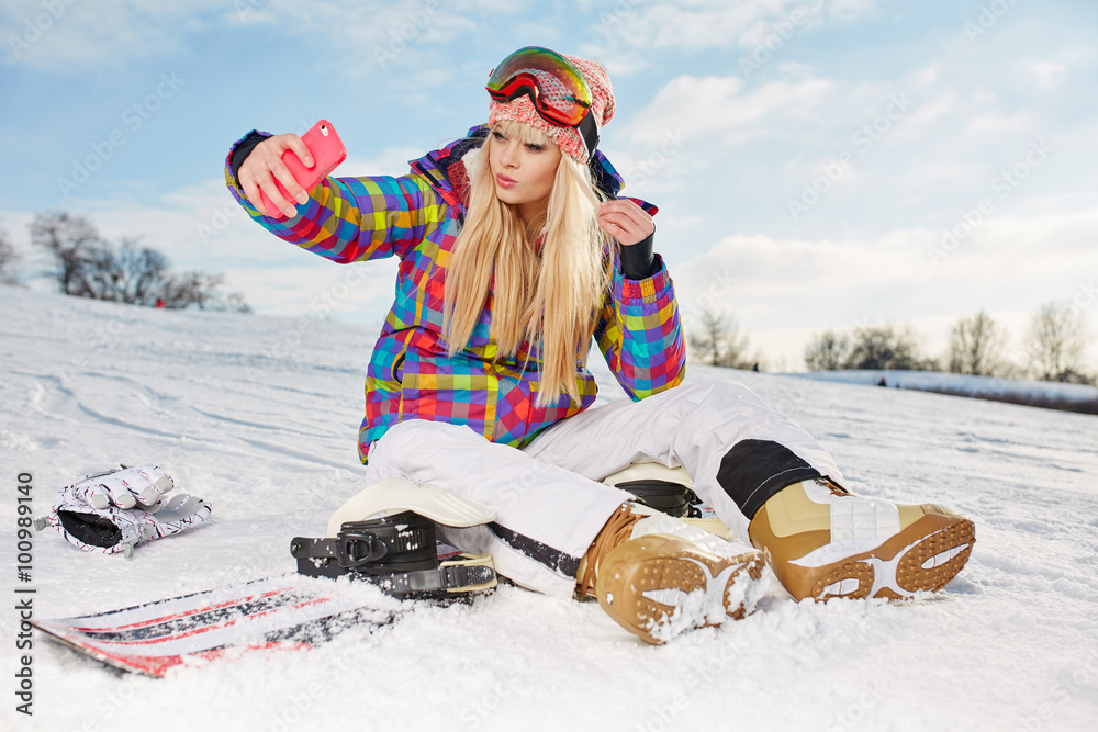  Girl with snowboard sitting on the snow and is making a selfie