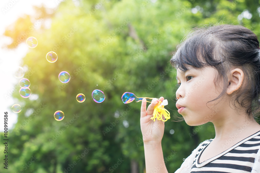 Asian little girl blowing soap bubbles in green park Asian little girl blowing soap bubbles in green park