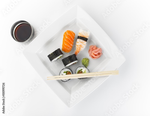 Top view of classic sushi set rolls with salmon and shrimp nigiris, wasabi, ginger, soy sauce and chopsticks on a white plate