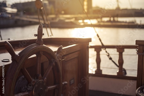 Steering wheel of an old wooden sailing ship in a port at sunset photo