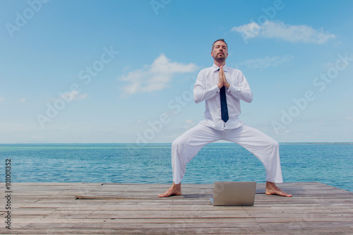 businessman doing yoga on a wooden bridge with a laptop
