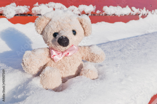 Cute teddy bear with pink necktie on snowy bench.