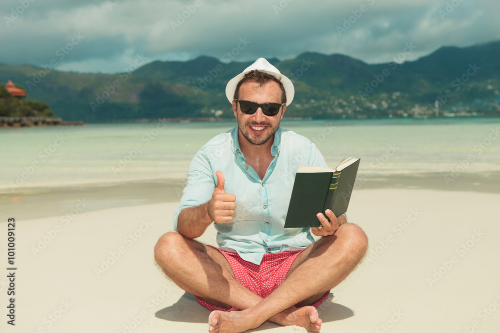 man sitting on the beach with book showing success sign man sitting on the beach with book showing success sign