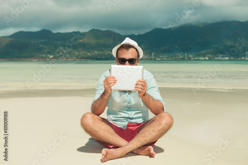 man wearing sunglasses hiding behind tablet while sitting legs c photo