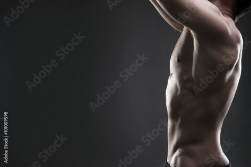 Handsome muscular bodybuilder posing on gray background. Low key studio shot with copy space