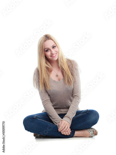 beautiful young woman with long blonde hair wearing a long sleeved cream shirt and gold necklace. sitting on the floor with legs crossed, isolated on white background.