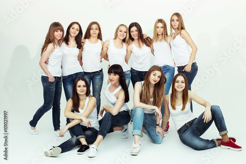 Happy together concept. Group portrait of healthy girls in white t-shirts and blue jeans sitting and posing over white background. Copy-space. Urban style. Studio shot