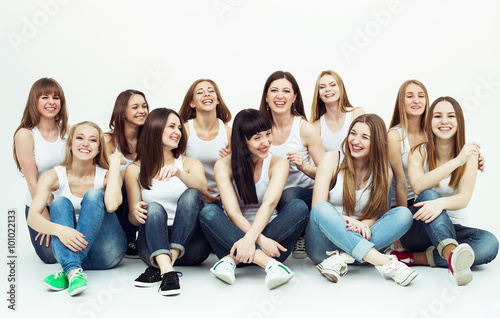 Happy together concept. Group portrait of healthy girls in white t-shirts and blue jeans sitting and posing over white background. Copy-space. Urban style. Studio shot