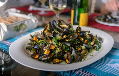 Mussels in a porcelain plate on a table against the background of a bottle of wine