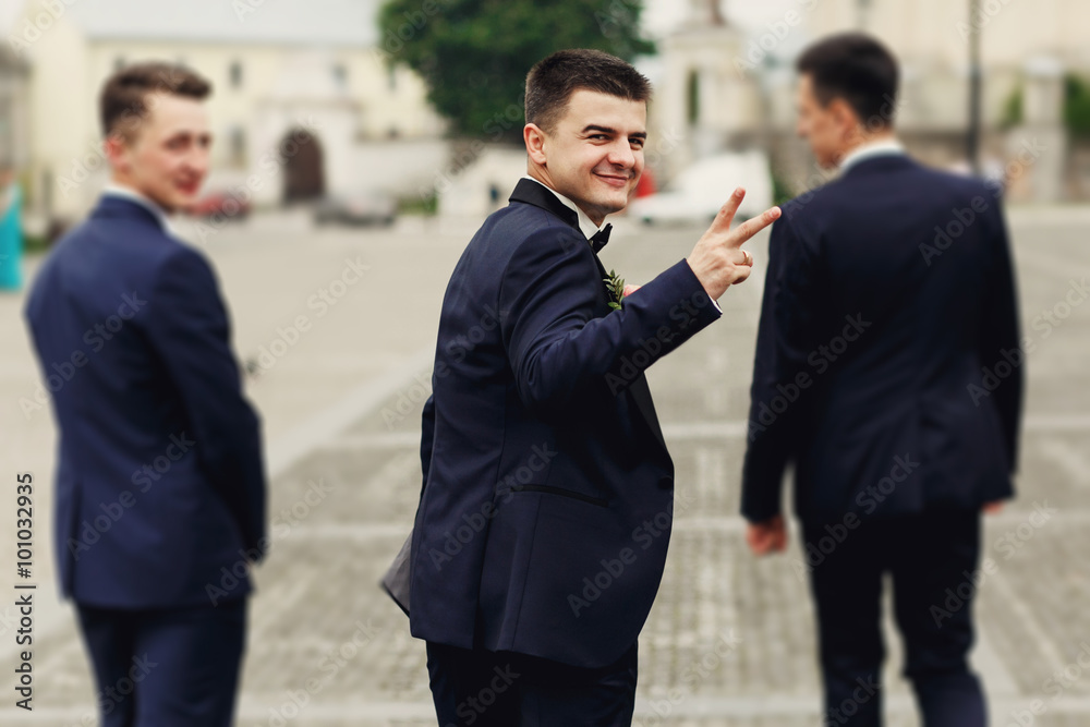 Confident smiling handsome groom in black suit with two groomsma Confident smiling handsome groom in black suit with two groomsma