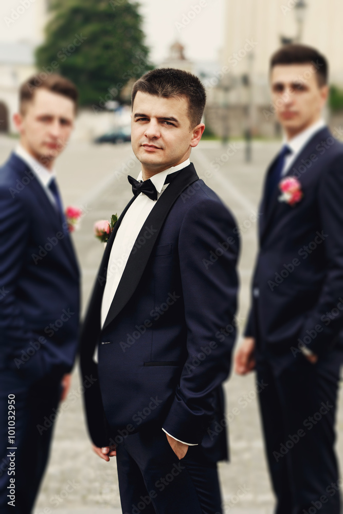Confident posing handsome groom in black suit with two groomsman Confident posing handsome groom in black suit with two groomsman