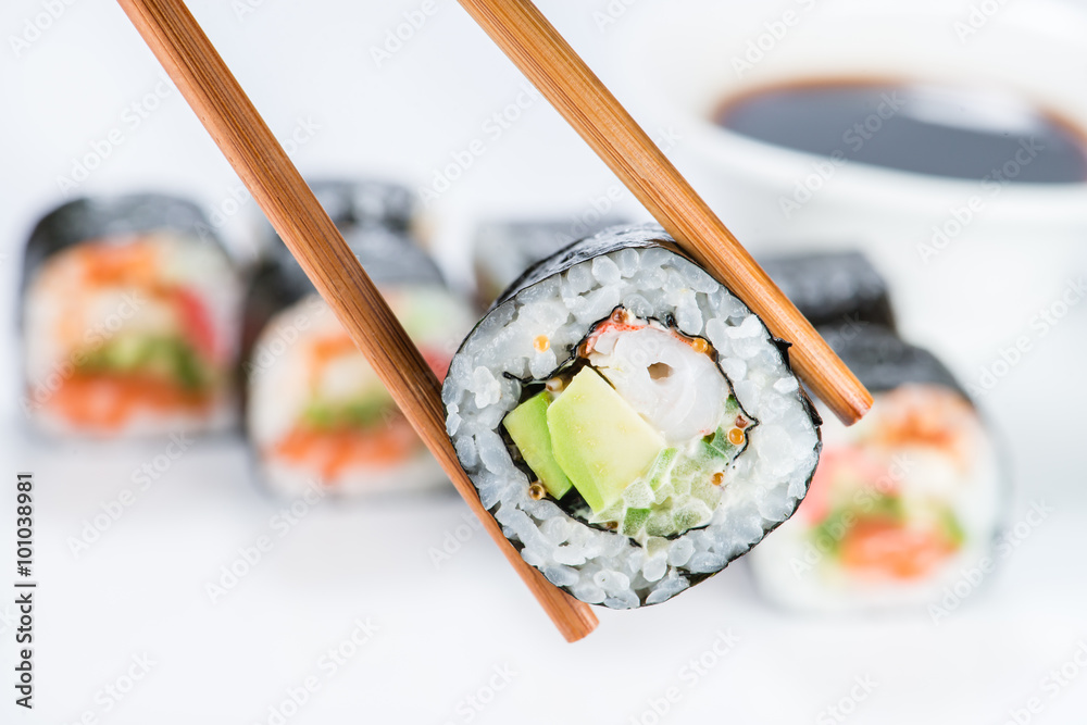 close up of chopsticks taking portion of sushi roll on the table close up of chopsticks taking portion of sushi roll on the table