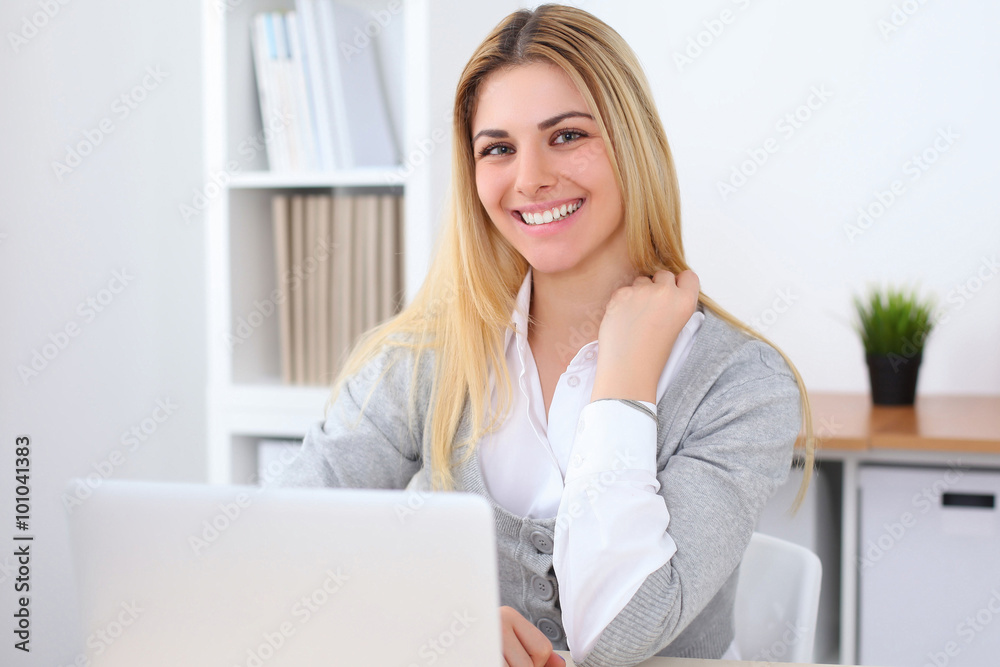 Portrait of young business woman sitting at the desk on office background