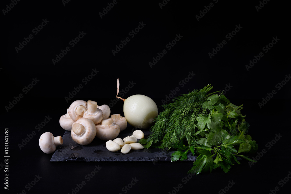 Young spring vegetables on slate board, black background. Champignon mushrooms, garlic, onion, dill, parsley and cilantro washed and prepared for cooking. Young spring vegetables on slate board, black background. Champignon mushrooms, garlic, onion, dill, parsley and cilantro washed and prepared for cooking.
