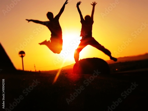 girl and boy silhouette jumping high on the sunrise 