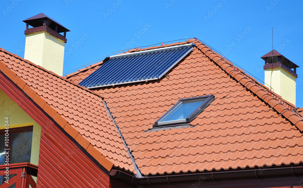 Energy efficiency concept. Closeup of solar water panel heating on red tiled house roof with lightning protection, skylights, chimney and roof window