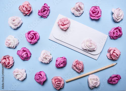 white envelope on a blue background with colorful paper roses and pencil top view close up