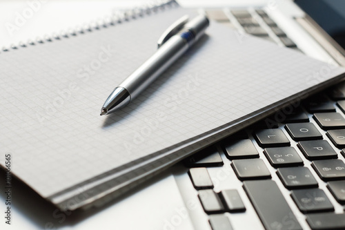 Laptop computer with notepad, pen on ivory table