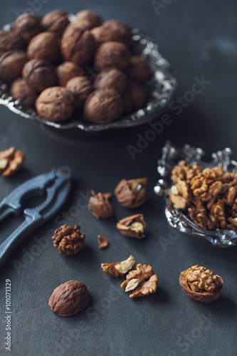 Walnuts in a bowl, whole and chopped on grey wooden table. Vintage style