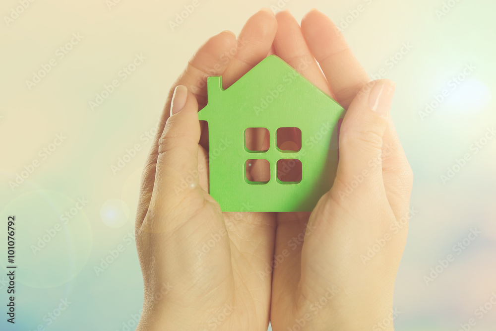 Female hands holding model of house on bright background Female hands holding model of house on bright background