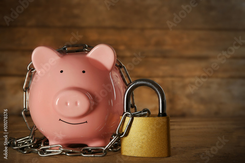 Piggy bank and chains on wooden background